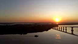 POR DO SOL COM BARCO E PONTE SILHUETADA NO GUAÍBA