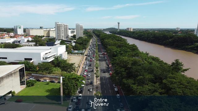 Avenida com grande movimentação mostrando rio e ponte estaiada.