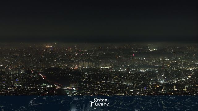 Cidade iluminada vista do alto à noite com poluição densa