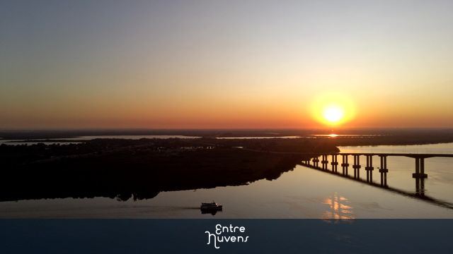 POR DO SOL COM BARCO E PONTE SILHUETADA NO GUAÍBA