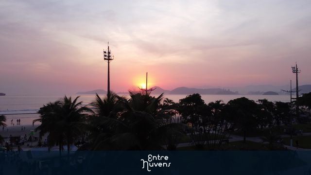 Pôr do sol em Santos - SP sobre a praia com palmeiras cheia de pessoas